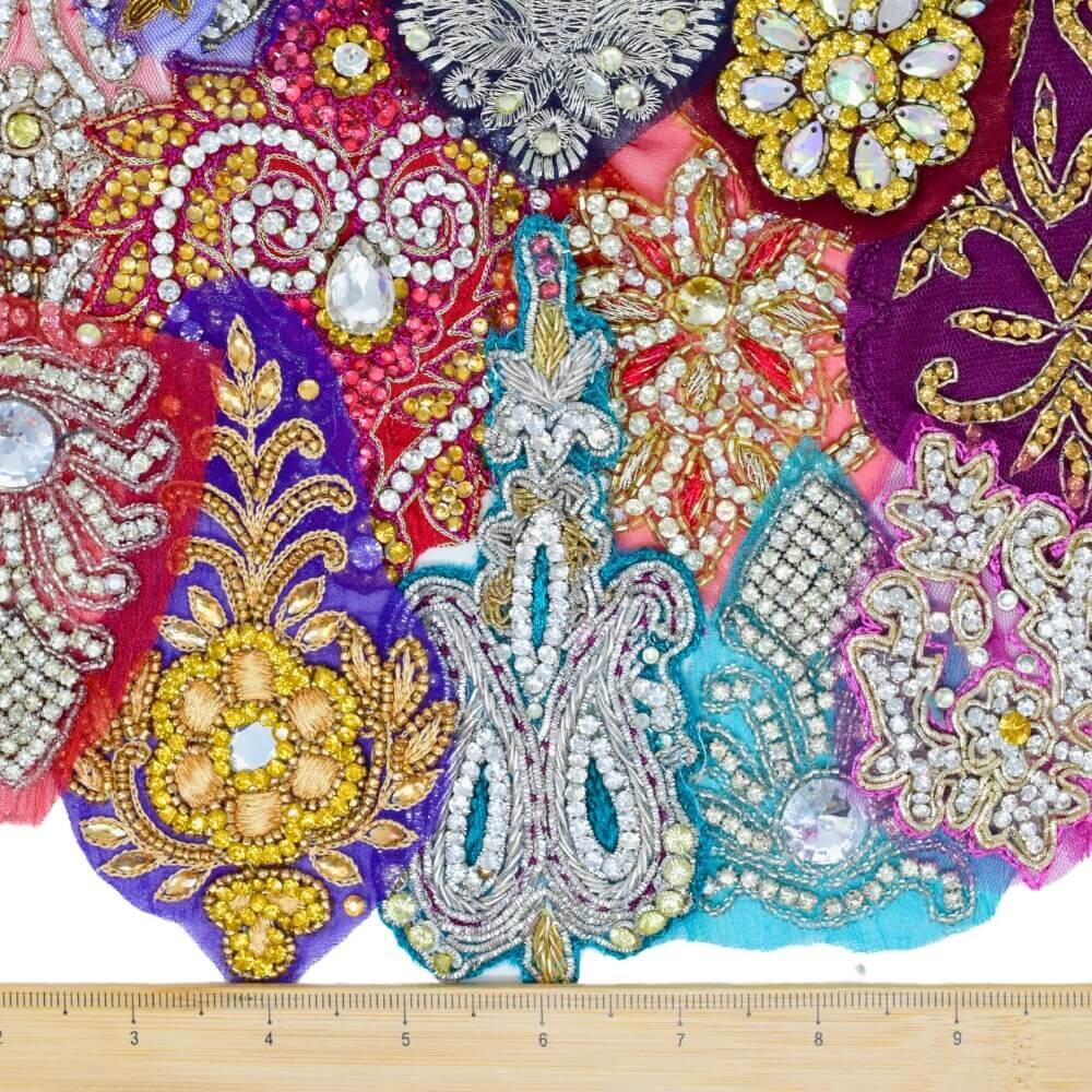 12 highly embellished and sparkly Indian motif fabricappliques with a wooden ruler placed along the bottom edge