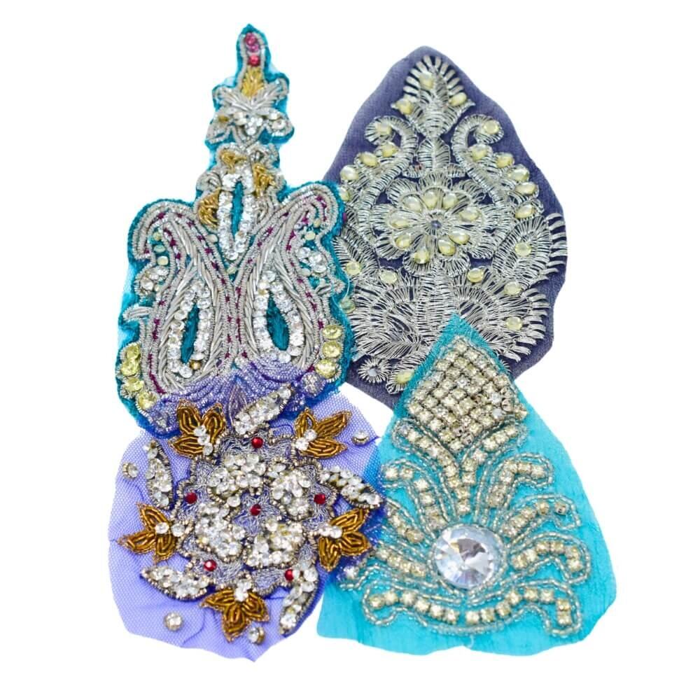 Flat lay of four blue highly embellished and sparkly Indian motif fabric appliques on a white background