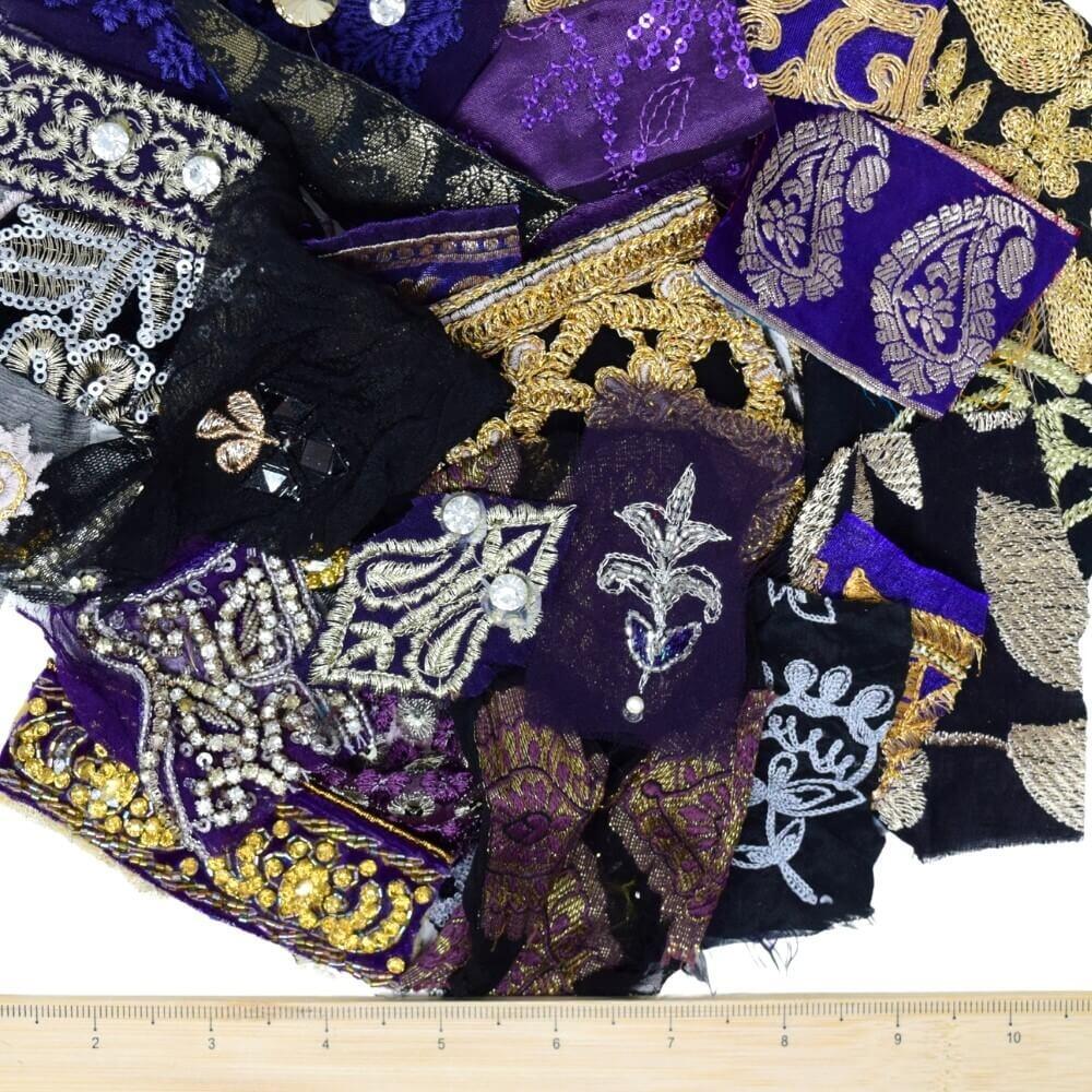 A selection of very small purple and black embellished sari fabric scraps with a wooden ruler placed along the bottom edge