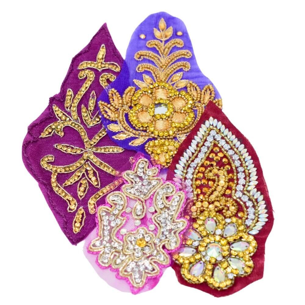 Flat lay of four purple highly embellished and sparkly Indian motif fabric appliques on a white background