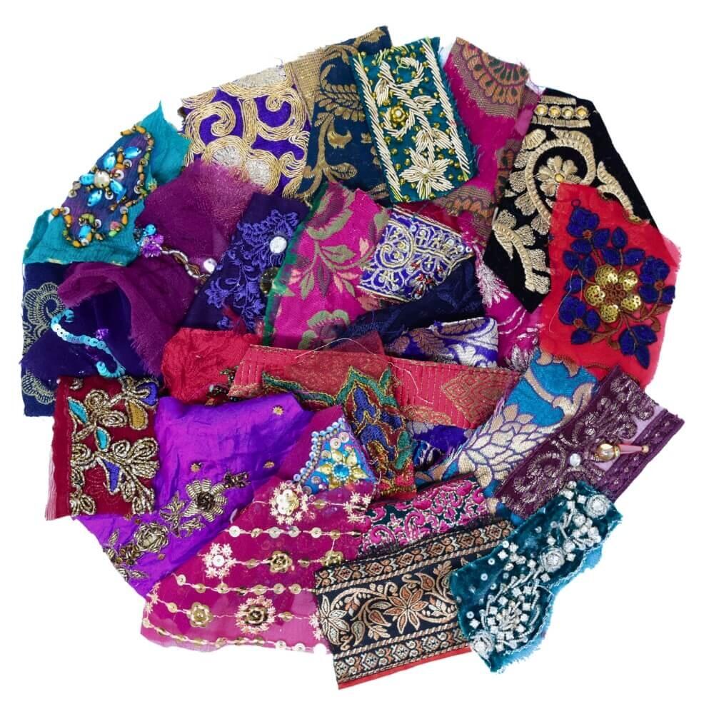 Flat lay of very small pieces of opulent coloured sari fabric scraps arranged in a rough circular shape on a white background