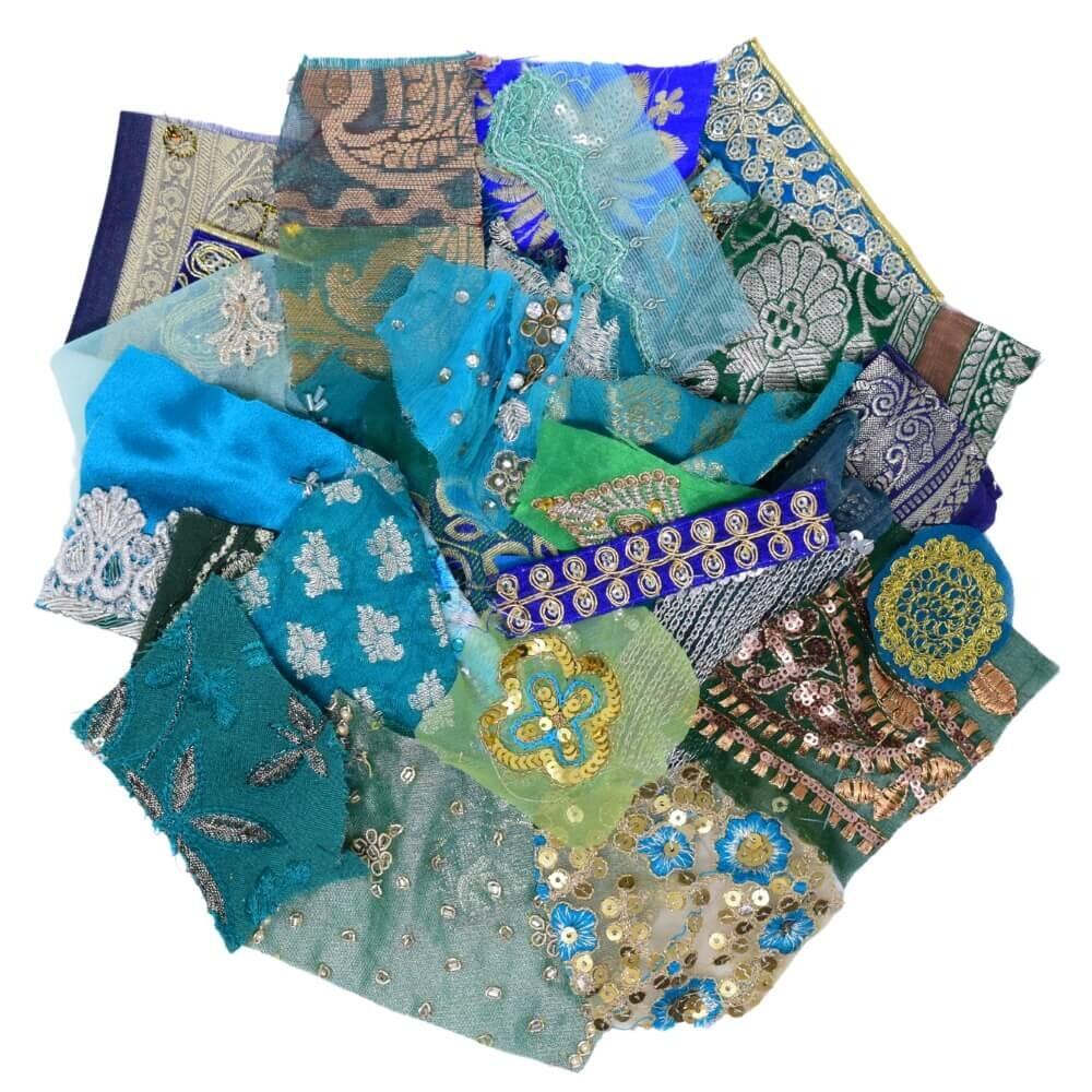 Flat lay of very small pieces of green and blue sari fabric scraps arranged in a rough circular shape on a white background
