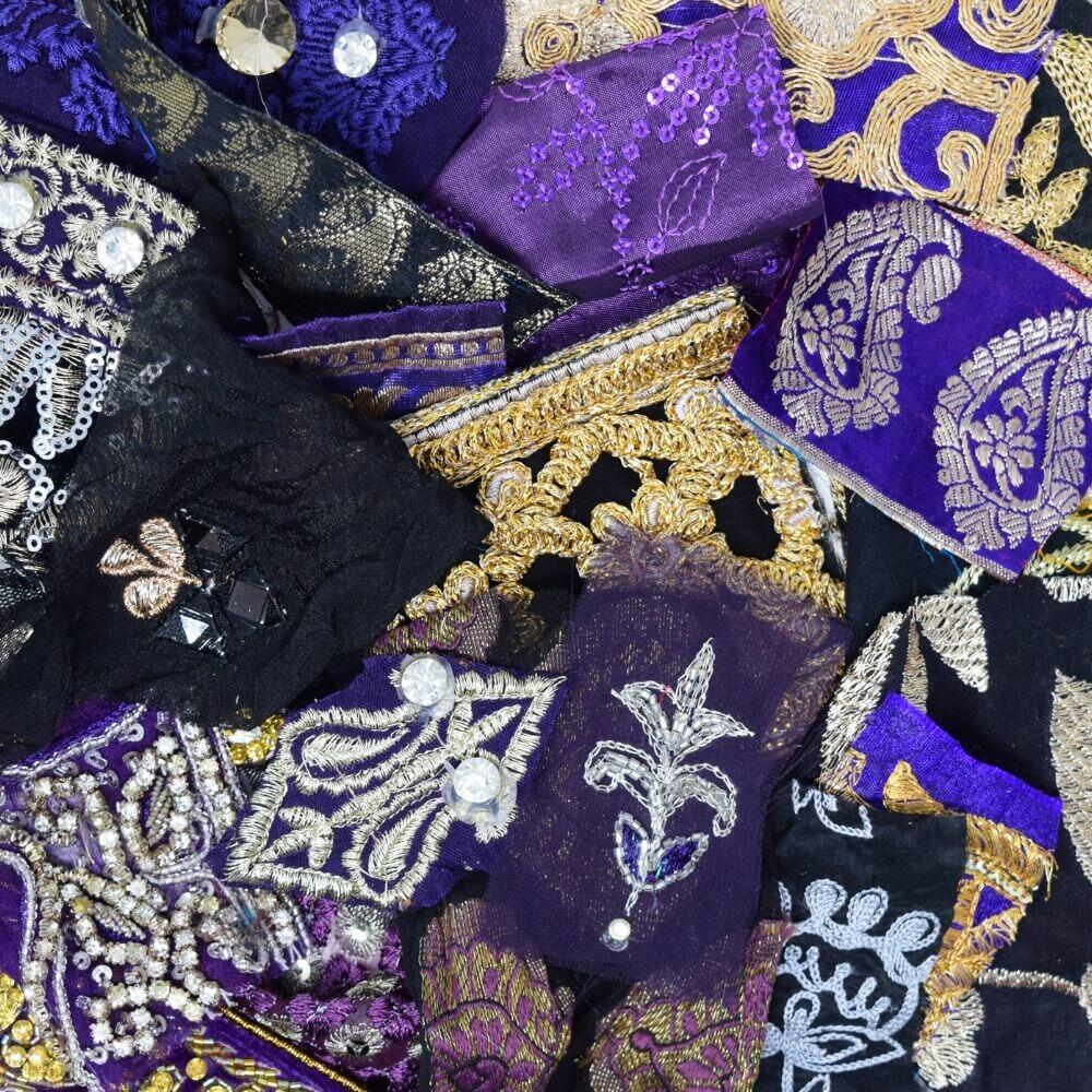 Flat lay of some very small pieces of embellished sari fabric scraps in a purple and black colour mix
