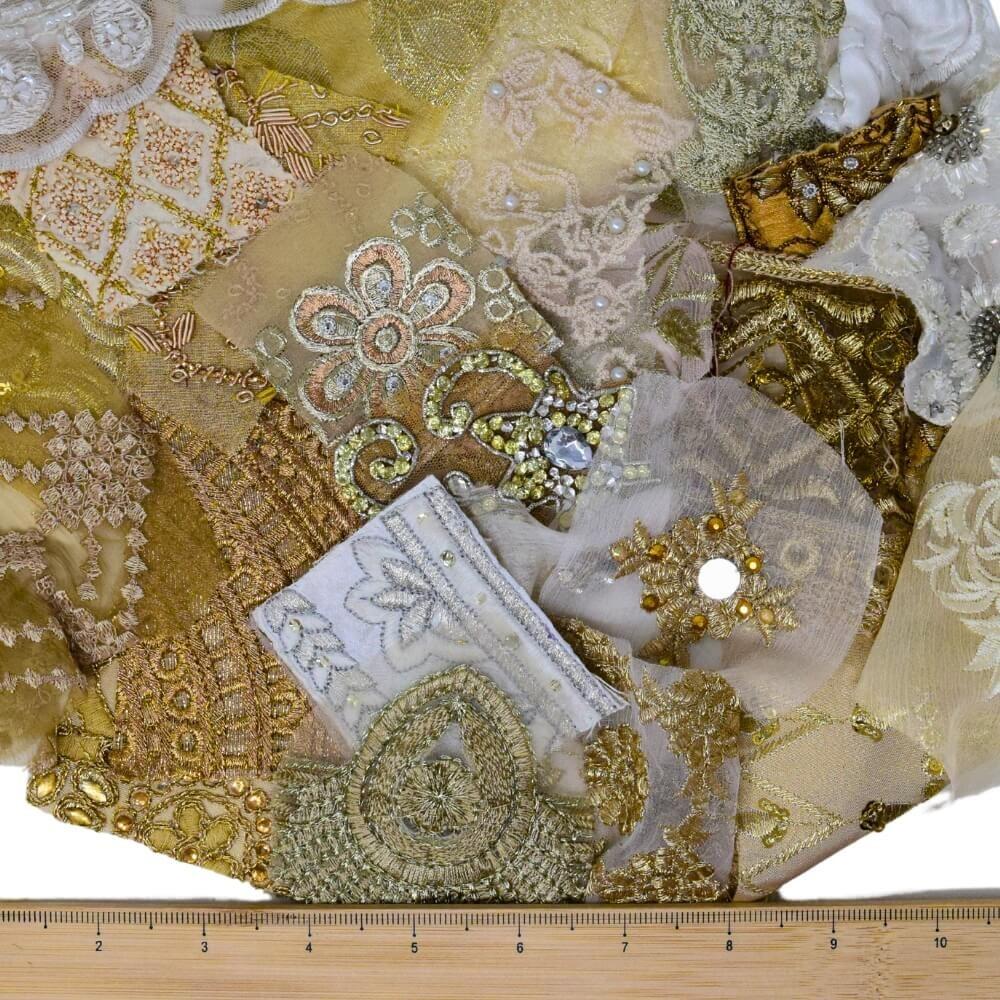 A selection of very small neutral coloured. embellished sari fabric scraps with a wooden ruler placed along the bottom edge