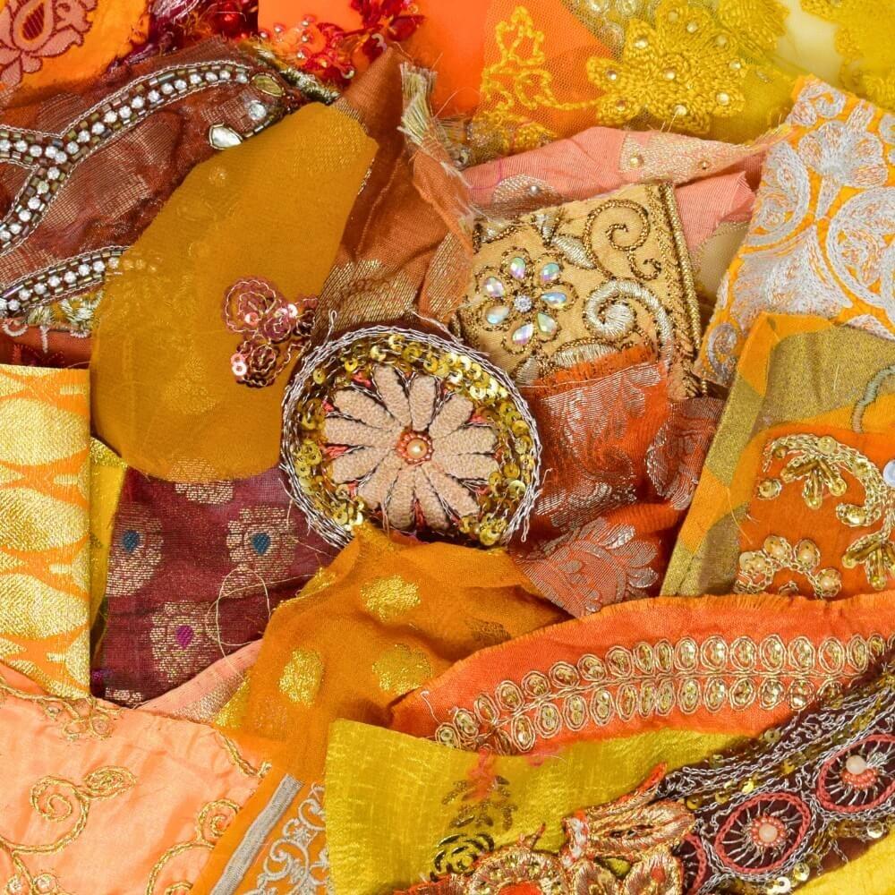 Flat lay of some very small pieces of embellished sari fabric scraps in a warm colour mix