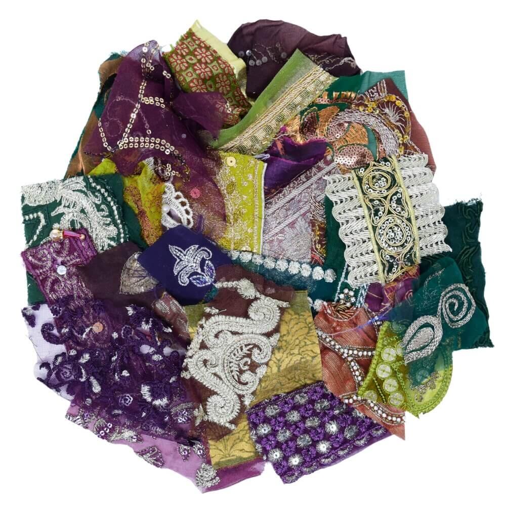 Flat lay of some very small pieces of green, purple and brown embellished sari fabric scraps arranged in a rough circular shape on a white background