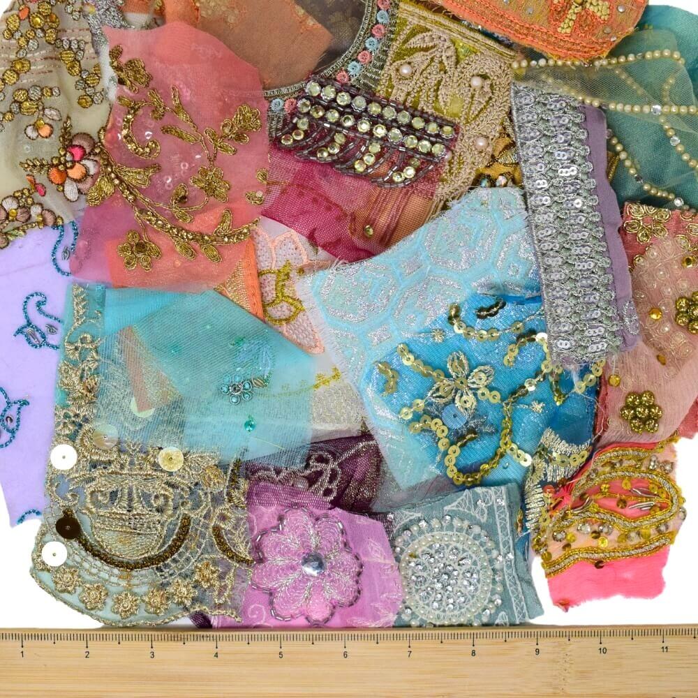 A selection of very small pastel coloured, embellished sari fabric scraps with a wooden ruler placed along the bottom edge