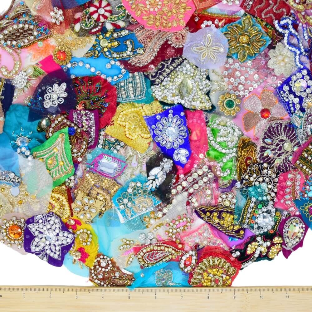 A large selection of sparkly sari fabric embellishment scraps with a wooden ruler along the bottom edge