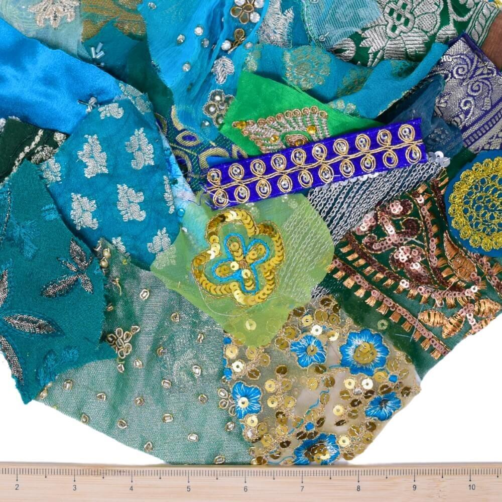 A selection of very small green and blue embellished sari fabric scraps with a wooden ruler placed along the bottom edge