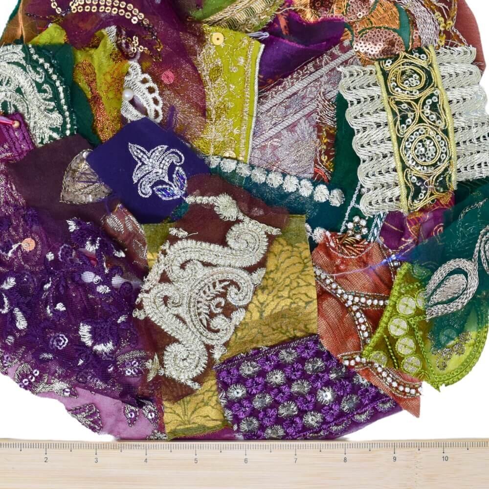 A selection of very small pieces of green, purple and brown embellished sari fabric scraps with a wooden ruler placed along the bottom edge