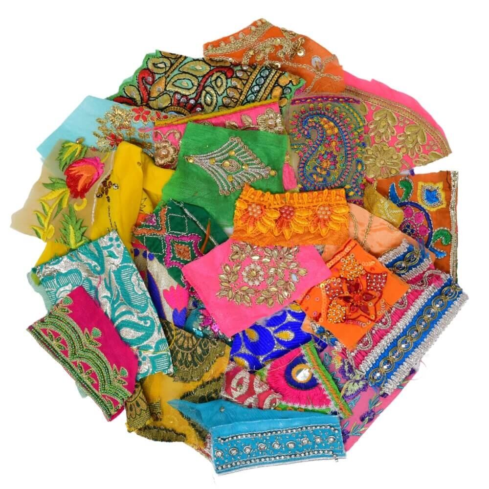 Flat lay of very small pieces of brightly coloured embellished sari fabric scraps arranged in a rough circular shape on a white background