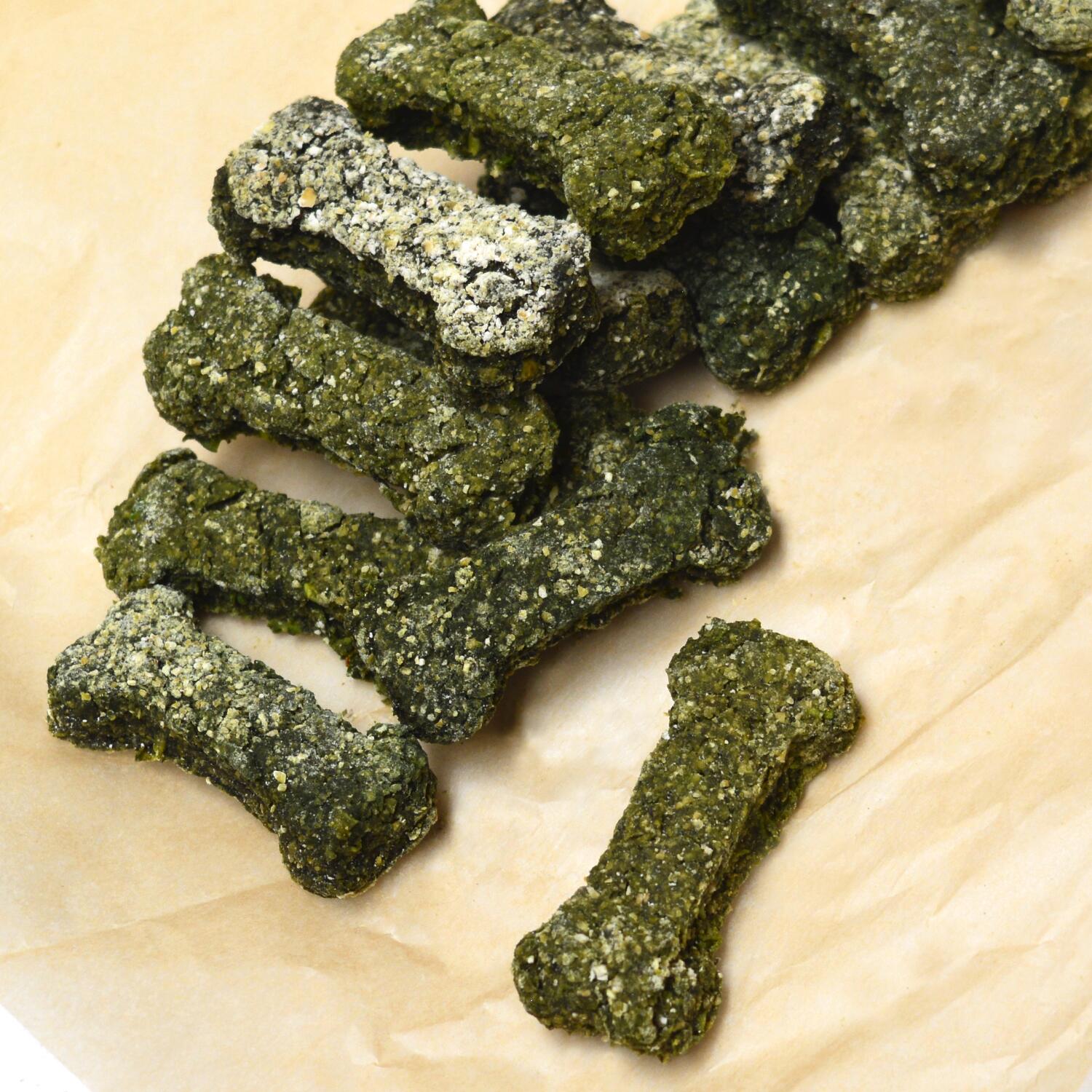 Booster Small Pea, Peanut Butter and Spirulina vegan bone shaped dog biscuits on brown parchment paper