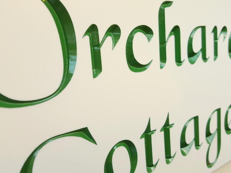 White engraved house sign with the house name Orchard Cottage inlaid with green paint