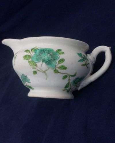Antique low round porcelain creamer or milk jug made by John Rose of  Coalport Porcelain Works with transfer printed and hand coloured turquoise and green flowers pattern. Dates to circa 1820.