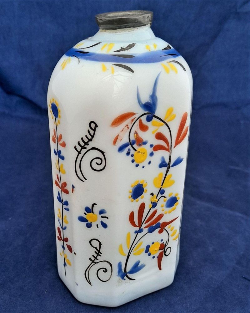 A George II period, circa 1740, mid 18th century antique Bohemian milk glass (milch glass) or opaque white glass spirit flask enamelled with floral scrolls. The decanter is made of opaque white blown  glass and has been formed by being mould blown in a dip or optic mould. The base has wear to the high points around the edges commensurate with an item of this age. It also has a rough or snapped pontil mark .