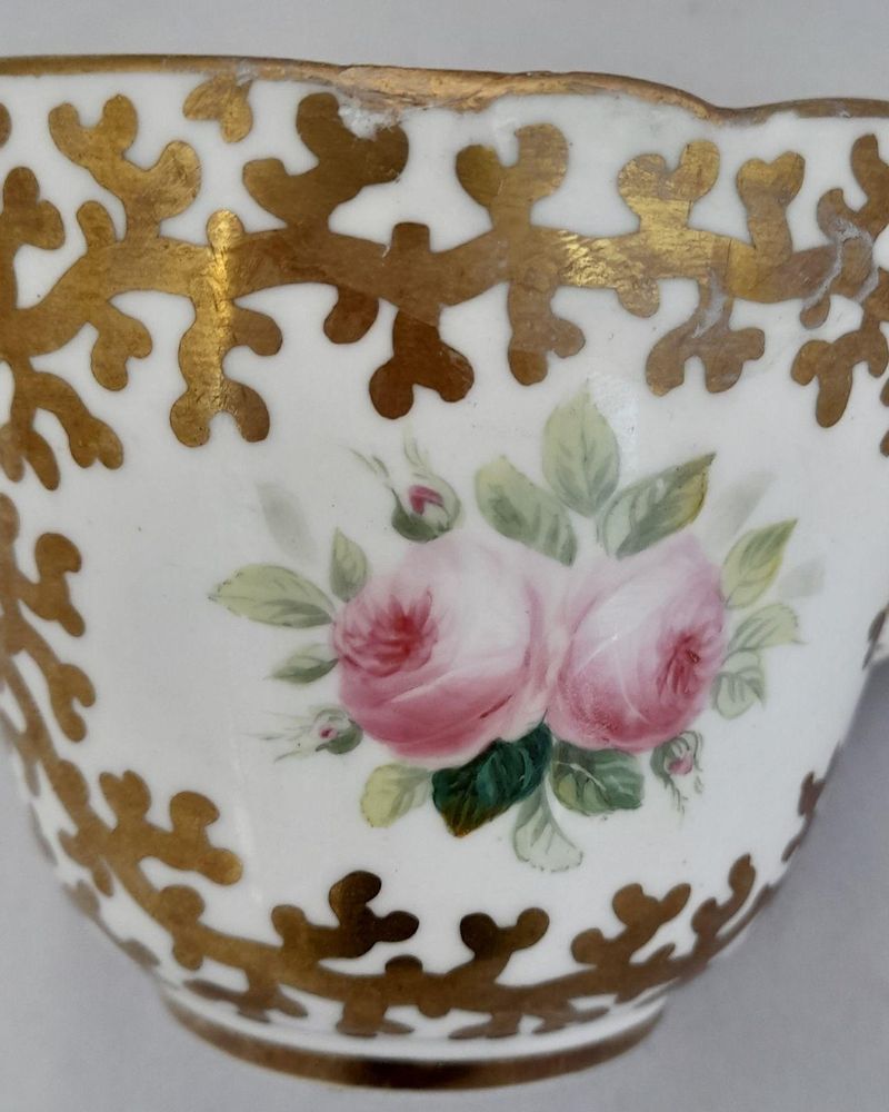 An antique mid Victorian porcelain tea cup and saucer with a scalloped rim and reinforced handle hand painted with roses and gilded extensively with a sea weed pattern made by Sir James Duke & Nephews circa 1860 in the factory previously run by Samuel Alcock and company.