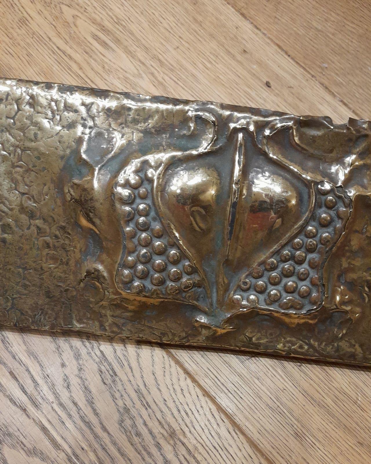 An antique brass Arts & Crafts or Art Nouveau repousse decorated fire fender or fire kerb decorated with stylised pomegranates and hearts circa 1900