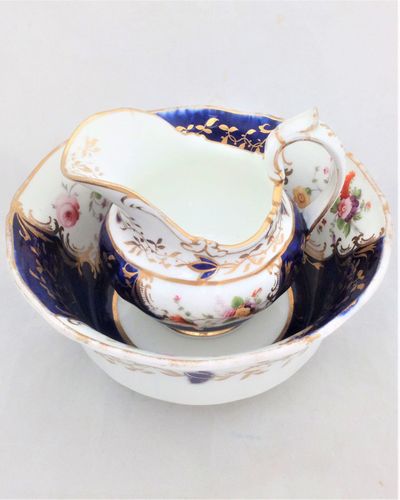 An antique john Rose of Coalport Bone China creamer or milk jug and bowl or slop basin both hand painted with flowers on a mazarine blue ground in pattern number 2 over 279 dating to circa 1830.