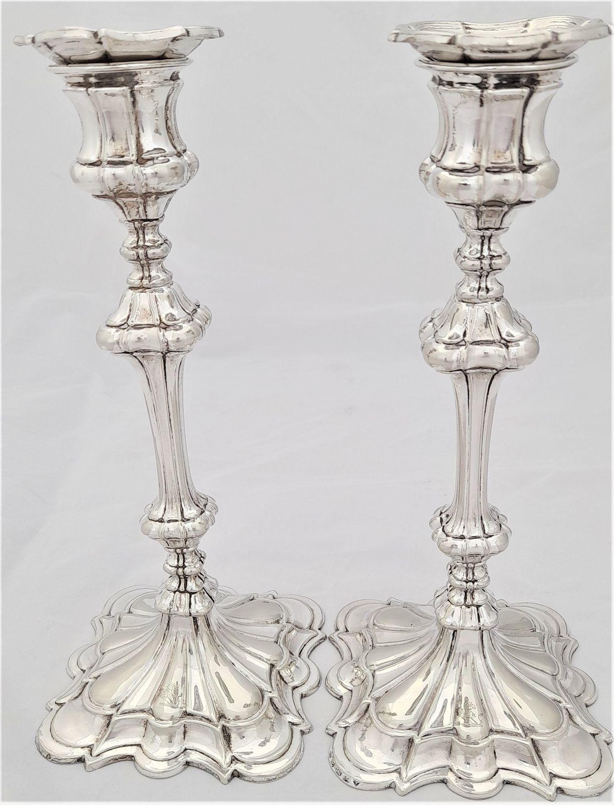 An antique pair of Elkington & Co silver plated candlesticks in the George III style marked with date code for 1854 with a family crest for Ripley  - demi lion holding a shield - square petalled weighted bases 10 inches high 1 kg weight for candles 7/8 inch diameter.