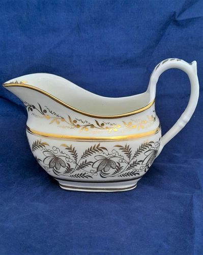 An attractive antique porcelain London shape creamer or milk jug decorated with gilded floriate pattern number 1149, featuring fronded leaves and stylised flowers on a white hybrid hard paste porcelain ground. The gilt pattern number 1149 is painted underneath. There is gilded lining or banding around the rim. The creamer was made by Thomas Rose of Coalport and dates to around 1812 during the Regency period of the later George IV.
