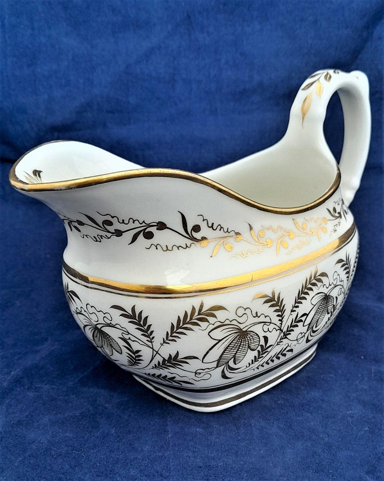 An attractive antique porcelain London shape creamer or milk jug decorated with gilded floriate pattern number 1149, featuring fronded leaves and stylised flowers on a white hybrid hard paste porcelain ground. The gilt pattern number 1149 is painted underneath. There is gilded lining or banding around the rim. The creamer was made by Thomas Rose of Coalport and dates to around 1812 during the Regency period of the later George IV.
