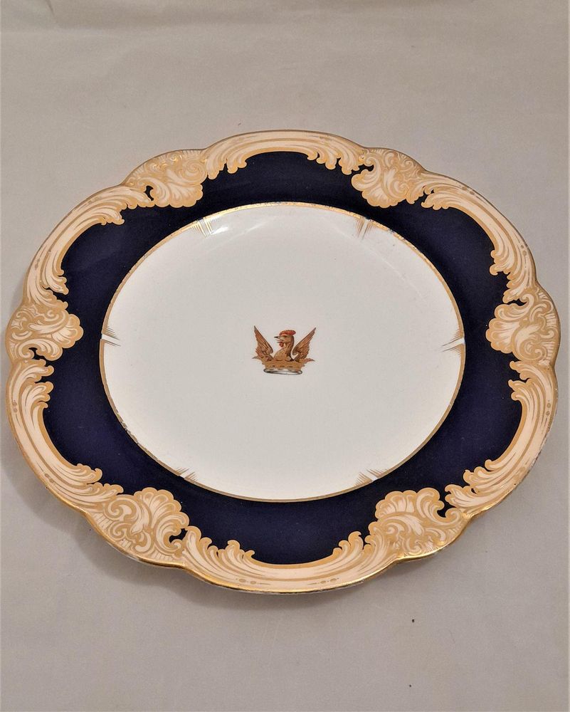 A very decorative 19th century armorial porcelain plate emblazoned with an heraldic crest for the family name Bellam, alternative spelling that the crest is also applicable to : Ballam, Bellome or Bellam .  A Heraldic description of the crest : Out Of A Ducal Coronet Or, A Cock's Head Between Two Wings Gu., Combed And Wattled Of The First.    The plate has an ornate under-glaze mazarine blue ground border and and gilded lobed rim which has an outer peach and gilded rococo scroll border. This beautiful quality plate dates from the mid 19th century circa 1850, the underside is unmarked without any maker's mark.