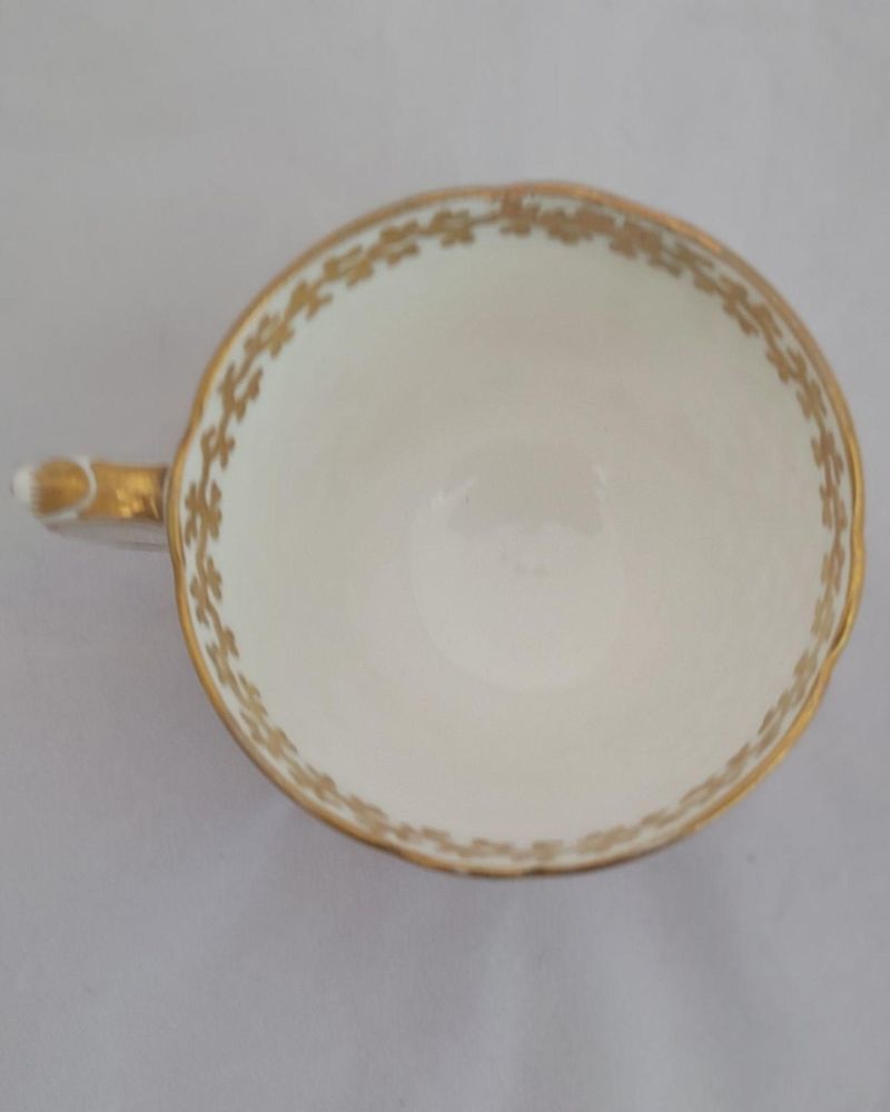 An antique mid Victorian porcelain tea cup and saucer with a scalloped rim and reinforced handle hand painted with roses and gilded extensively with a sea weed pattern made by Sir James Duke & Nephews circa 1860 in the factory previously run by Samuel Alcock and company.
