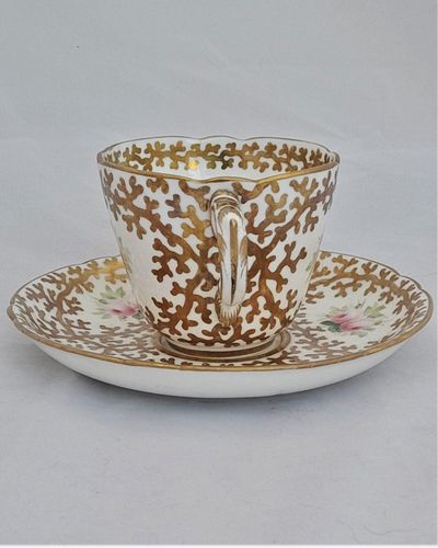 An antique mid Victorian porcelain tea cup and saucer with a scalloped rim and reinforced handle hand painted with roses and gilded extensively with a sea weed pattern made by Sir James Duke & Nephews circa 1860 in the factory previously run by Samuel Alcock and company.