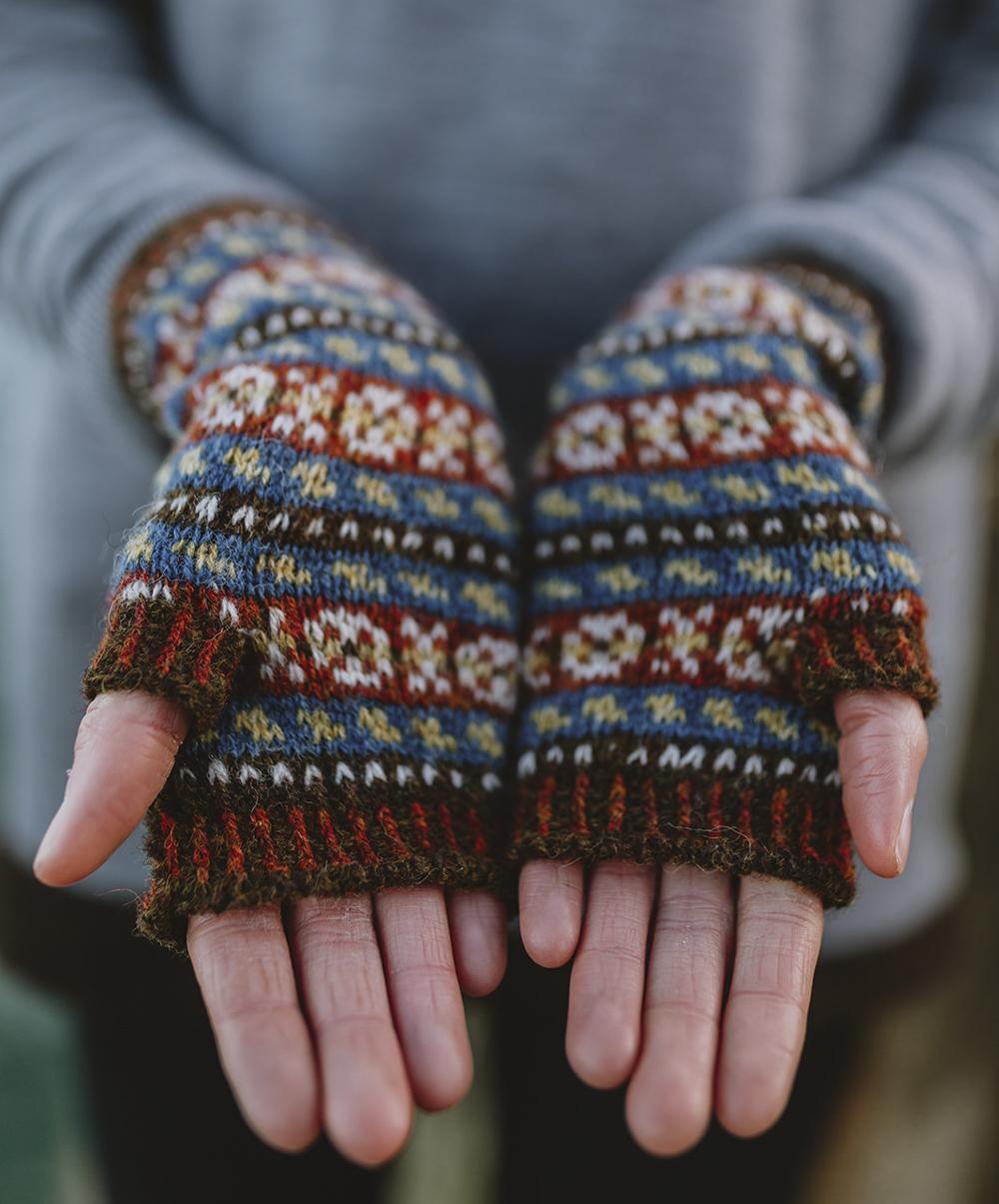 Hesti Mitts - hands are open to reveal a pair of fingerless mitts featuring small (peerie) patterns in the traditional palette of dark reds, indigo blues, golds and browns and greys used by Shetlanders prior to widespread availability of synthetic dyes