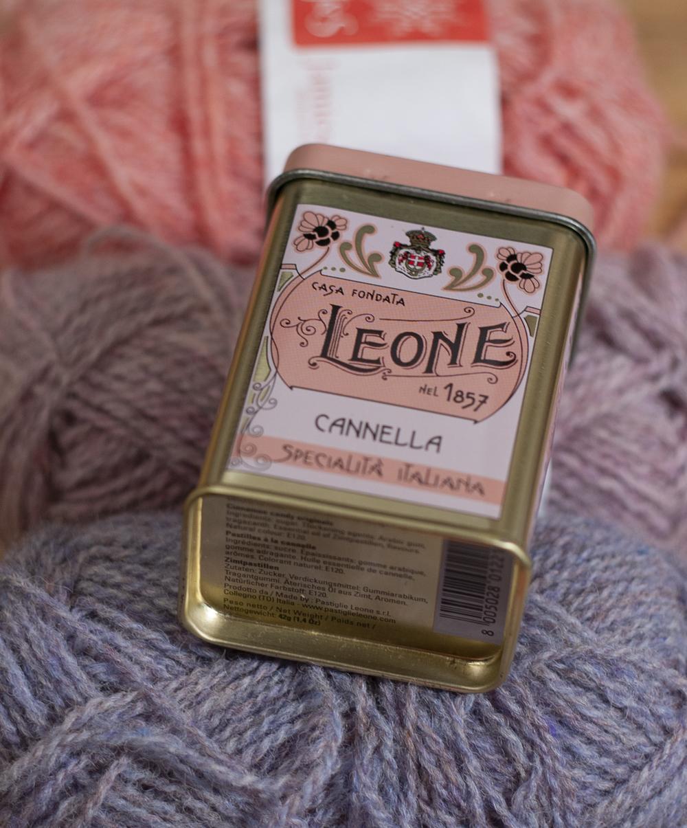 my inspiration source - a cinnamon pastilles tin in shades of lilac, pink and rose gold; pictured here on a collection of yarns in representative shades