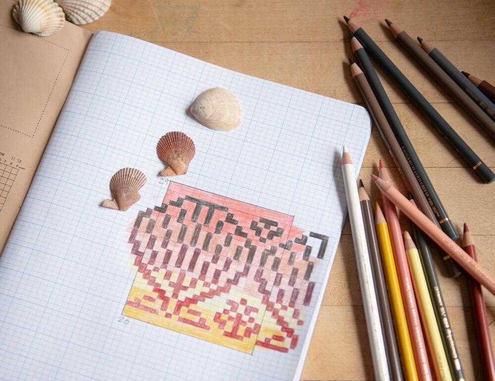 closeup of Knitters Graph Paper Journal with an exciting shell motif charted out in it, along with the shells that inspired this, and some lovely coloured pencils that speak to their pinky brown shades