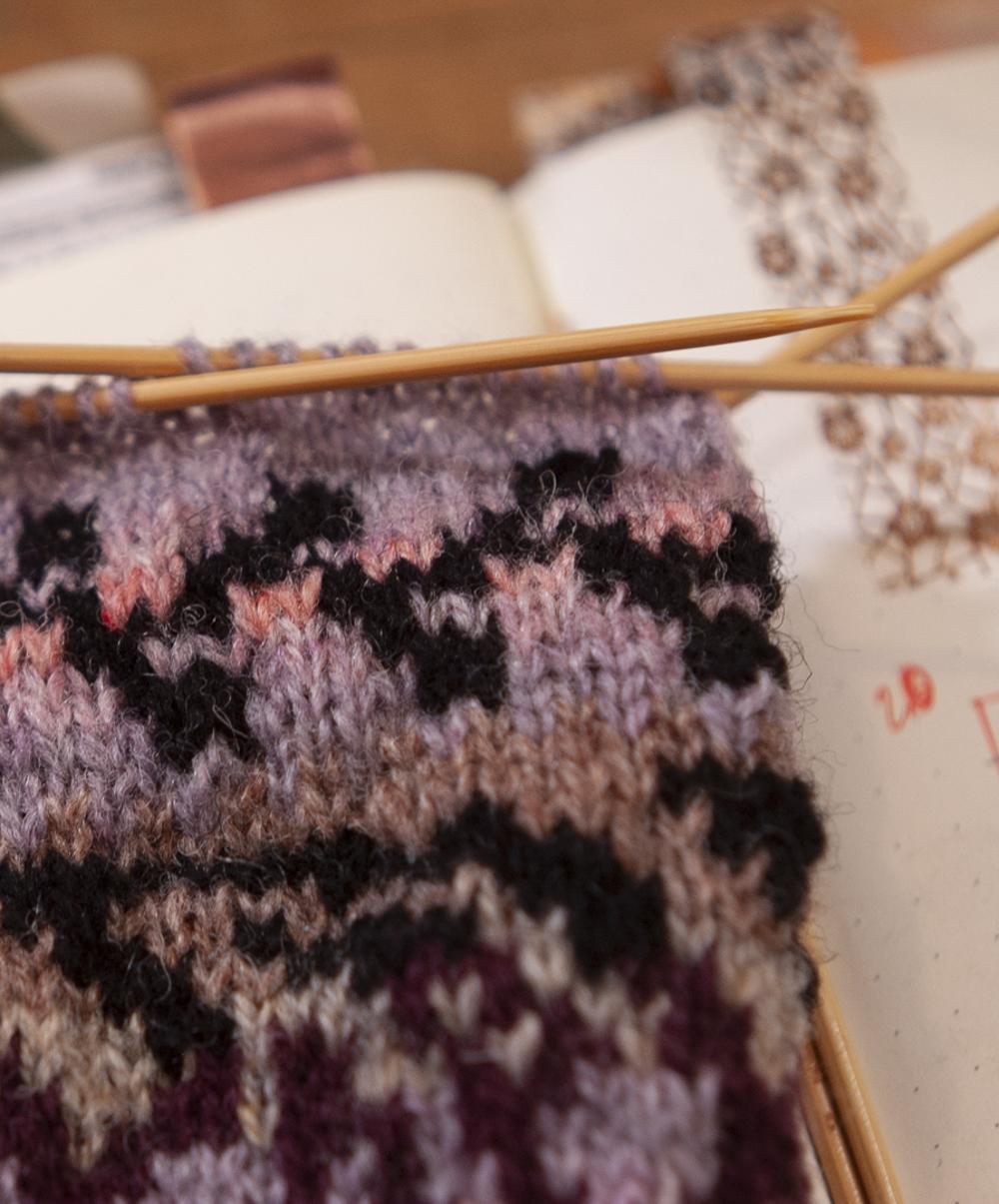a swatch on the needles - the lilac, pink and black yarns picked out to represent the tin are being knit here in patterns that speak to design details on the inspiration source