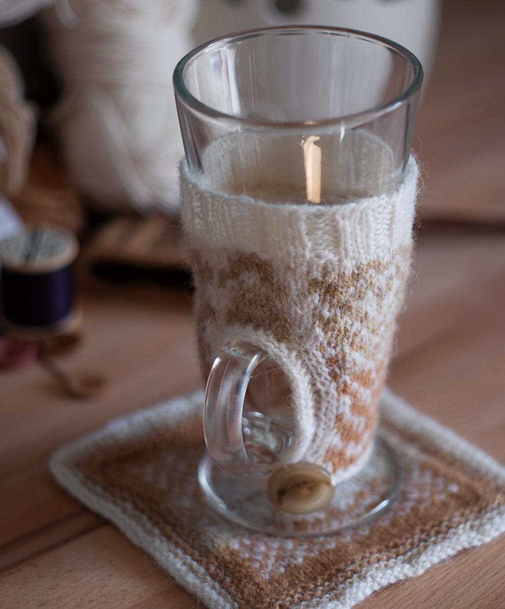 Latte glass covered in latte-art inspired stranded colourwork woolly cosy, with matching woolly coaster.