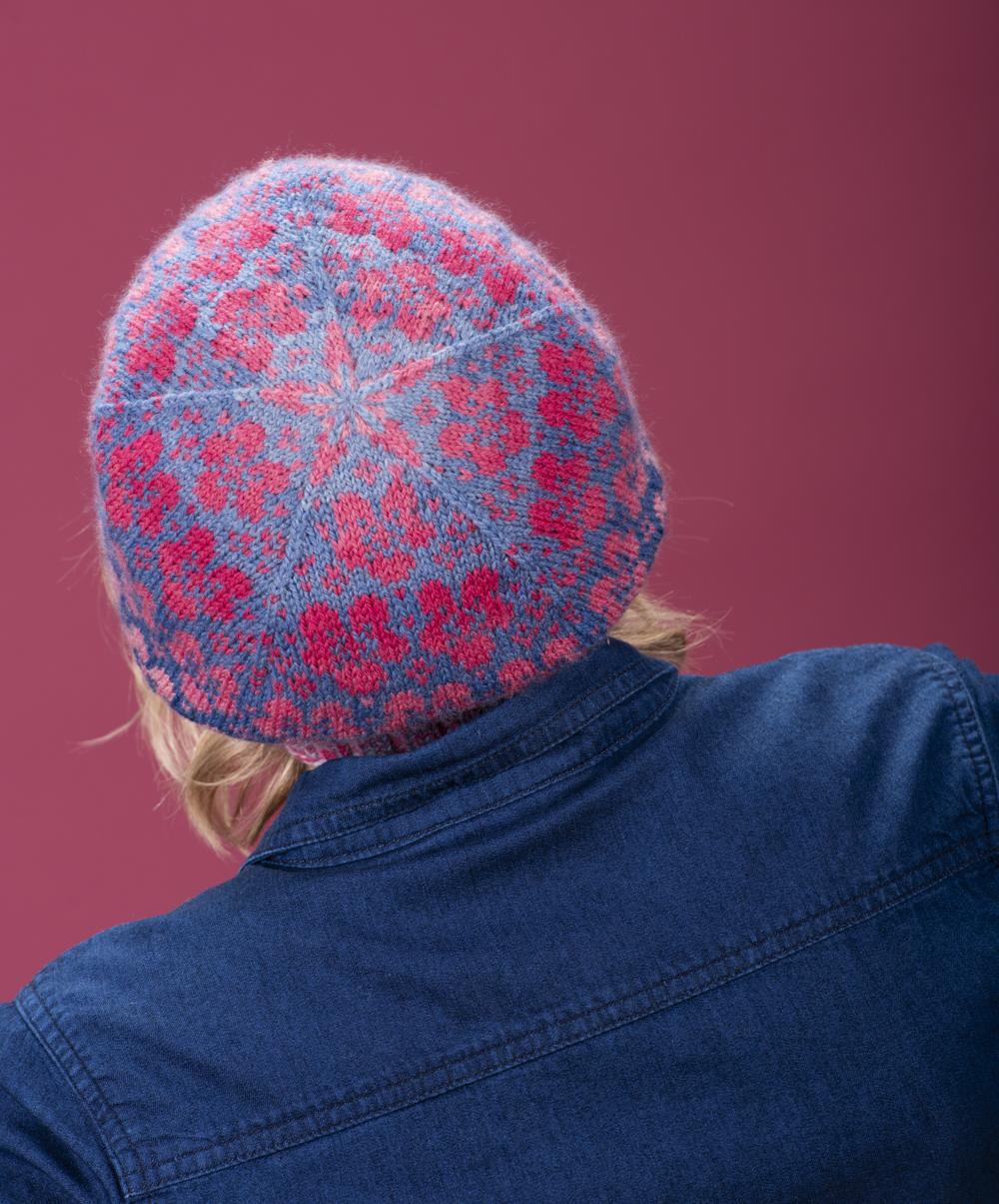 Heidi faces away from the camera so that we can only see the crisp patterning on the crown of the Flombre hat, which stands out as a geometric pink form against a blue background; the background of the photo is pink and Heidi wears a deep blue denim dress