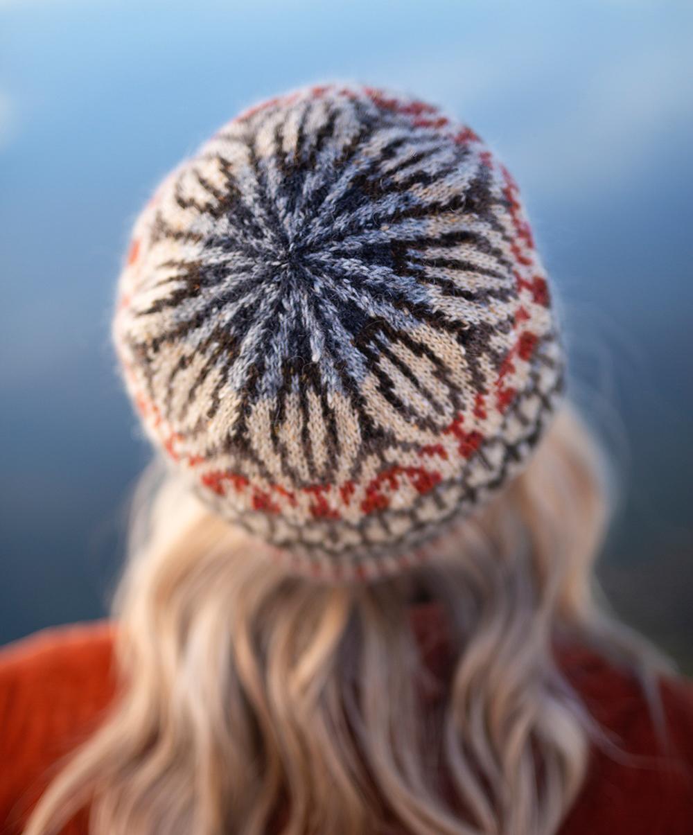 Jane Hunter Models Featherheid - a stranded colourwork hat design based on duck plumage; the background is blue with lochs and skylines