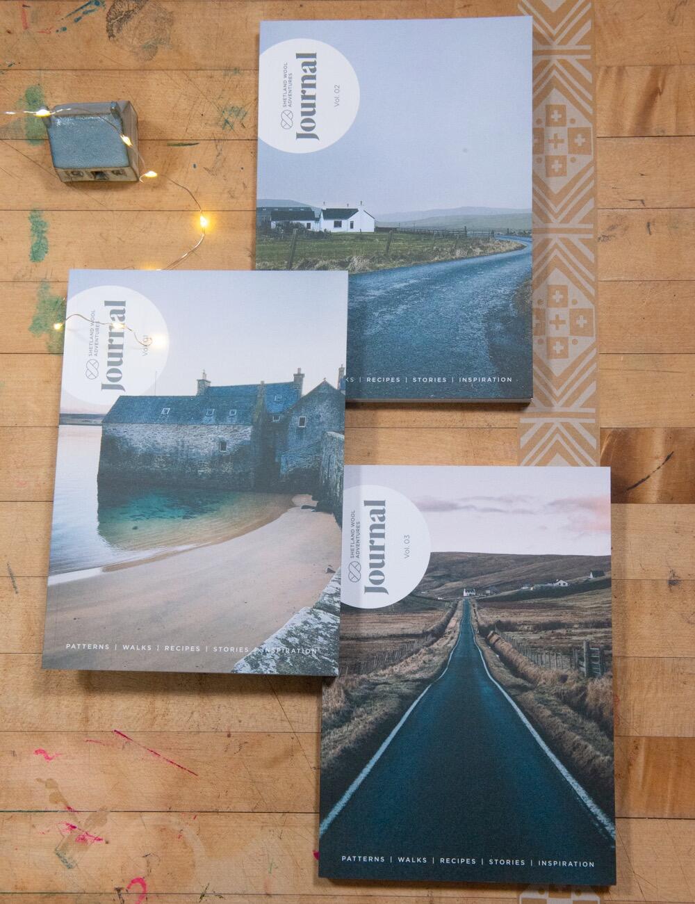 Shetland Wool Adventures, Volumes 1-3 arranged on a table and accompanied by fairy lights and miniature Shetland Crofthouses