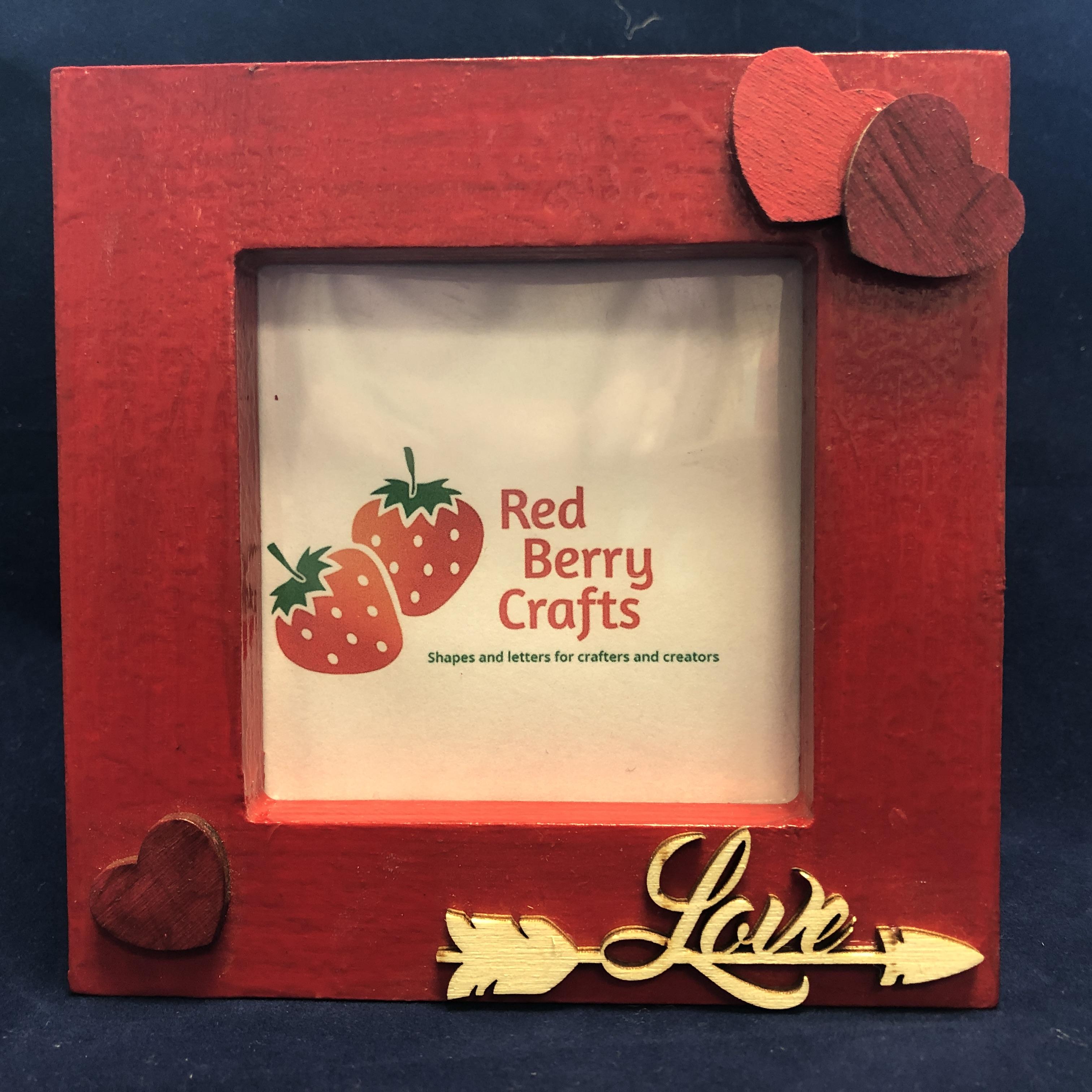 Wooden photo frame, painted red with wooden heart shape and a love arrow embellishments on the front.