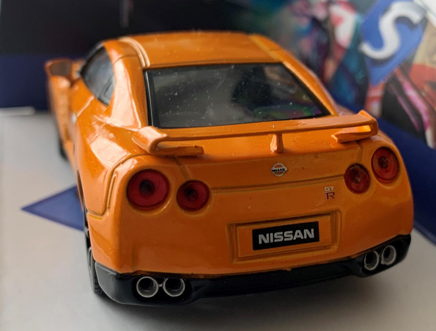 An accurate replica of a Nissan GT-R from 2007 decorated in orange with rear spoiler and black wheels.