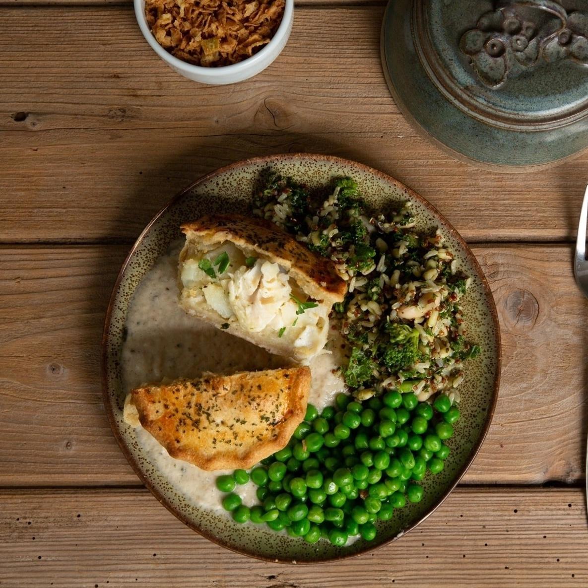Cullen skink pie cut in half and served with potatoes and peas