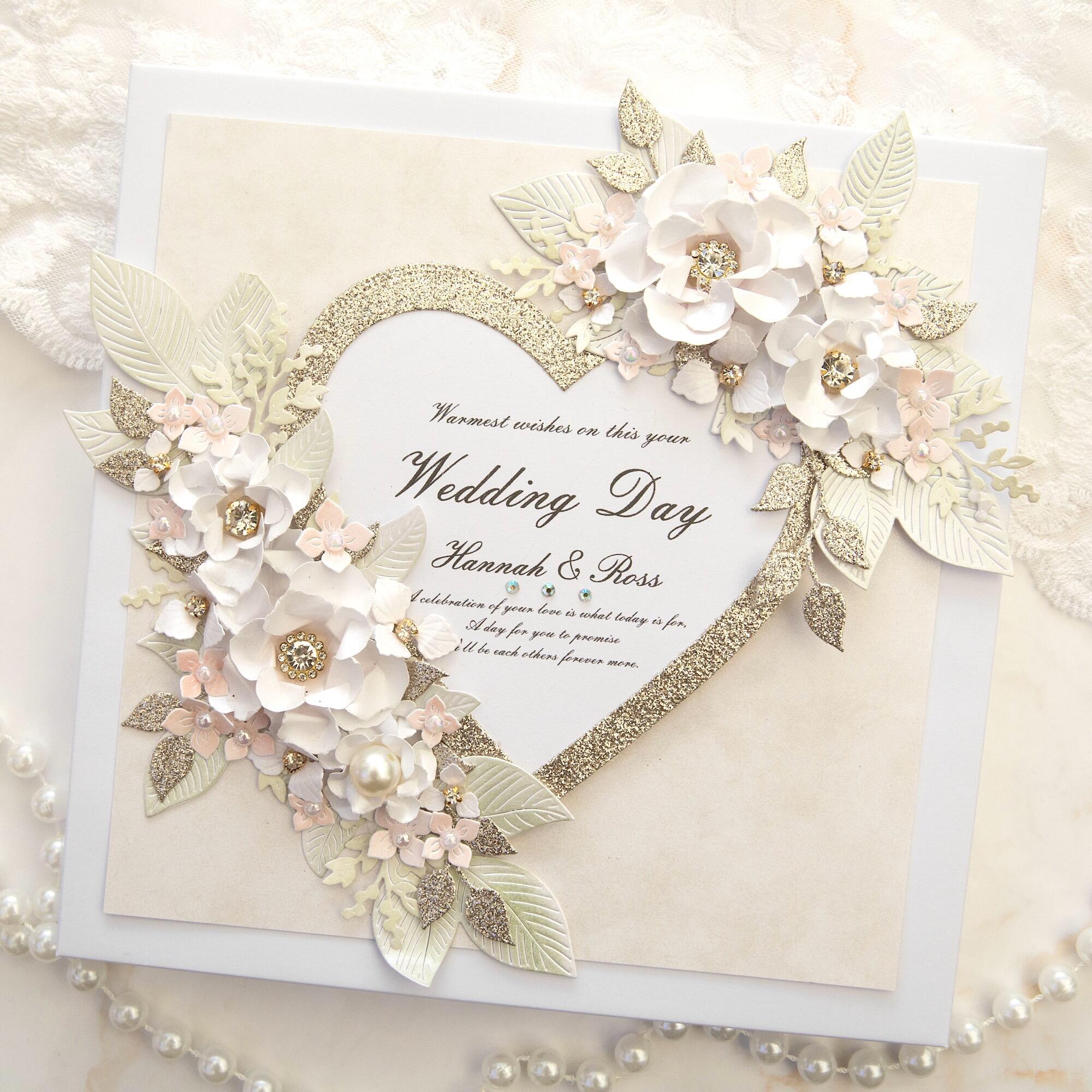 Luxury handmade personalised 8x8 wedding card with gold glitter heart outline reading Warmest wishes on this your Wedding Day Hannah and Ross, decorated with 3D handmade white and blush pink flowers with crystal diamante centres, pearls and sage green leaves
