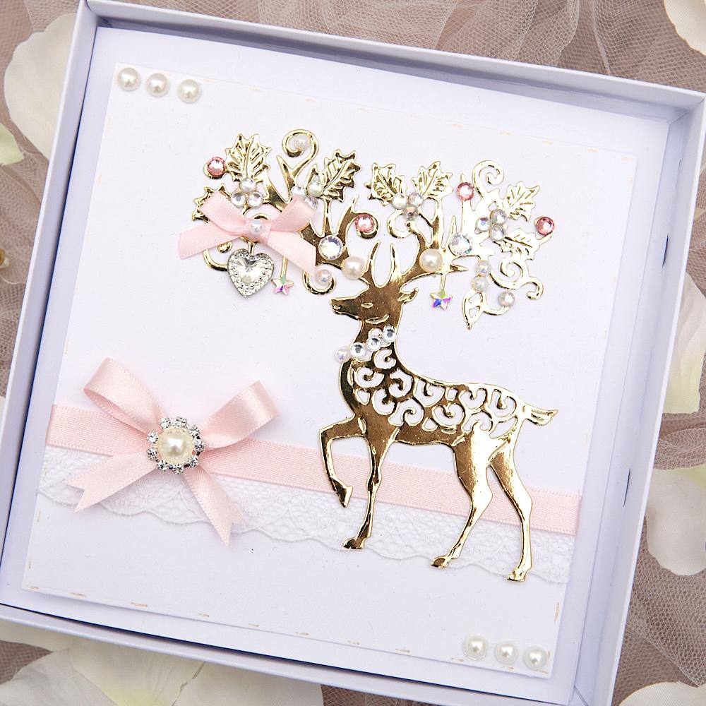 A boxed Christmas card against a wooden background featuring stag embellishment and ribbon bow