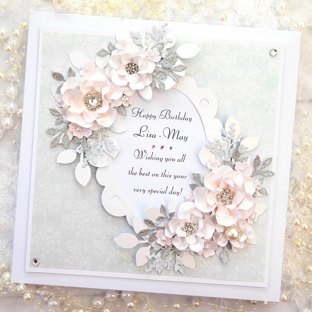 A square greeting card sits against a white lace background covered in ivory and white pearls