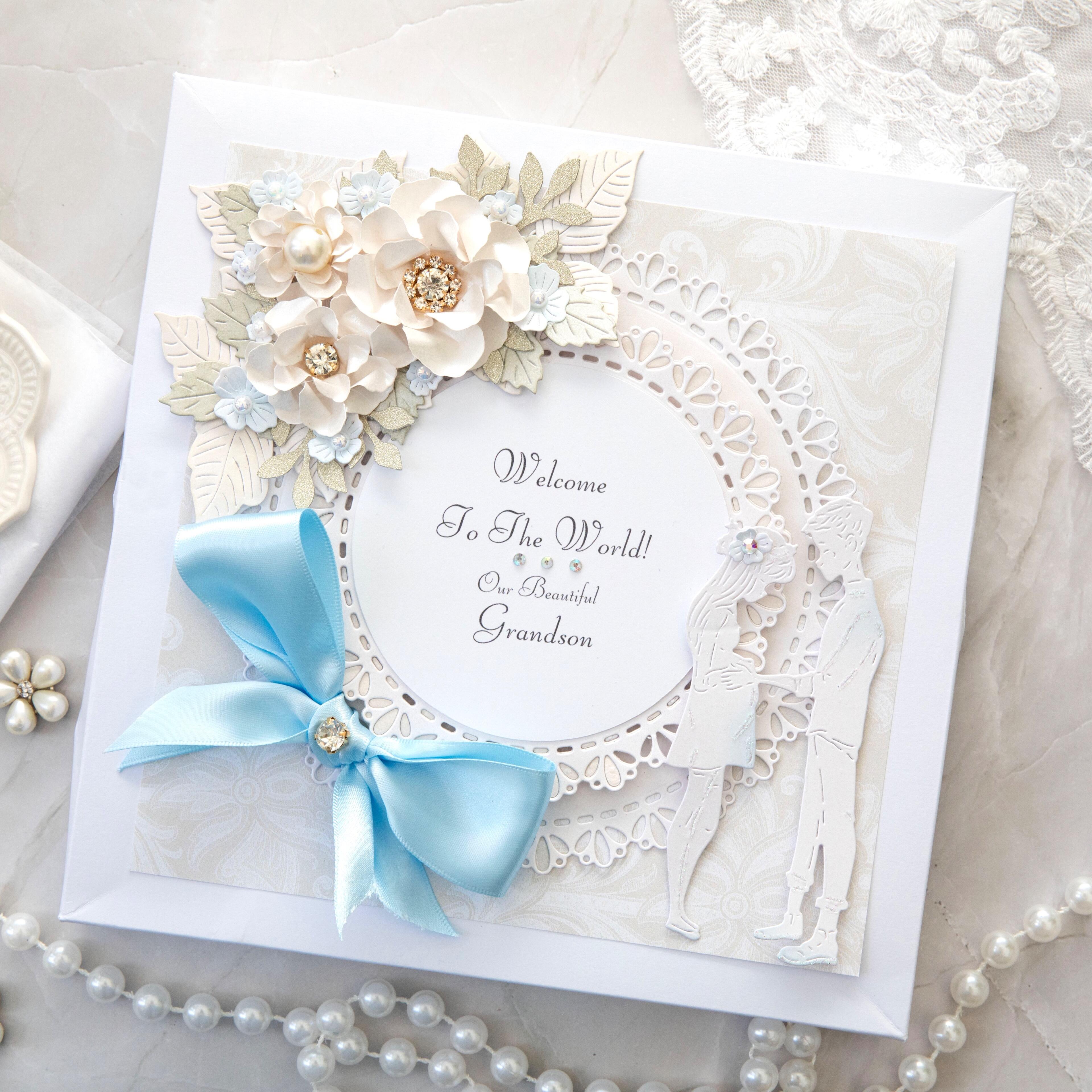 A square greeting card sits against a white lace background covered in ivory and white pearls