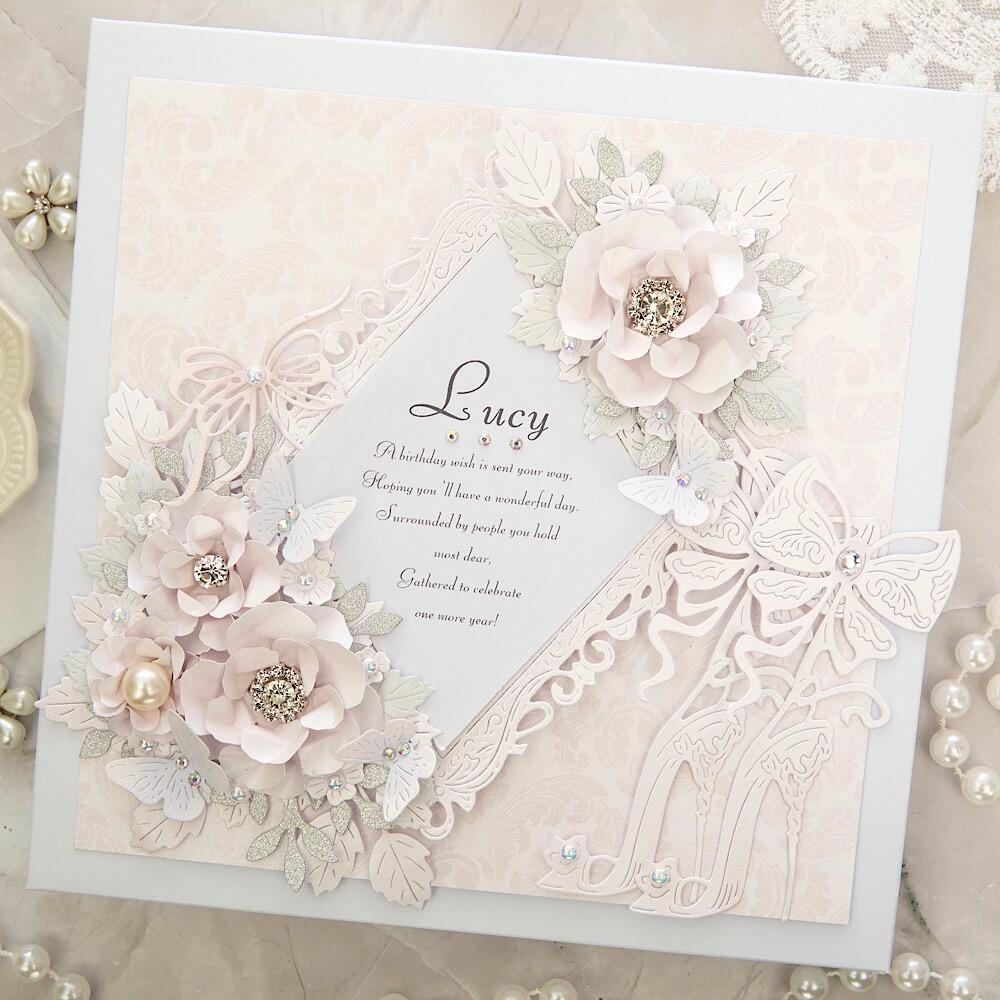 A square greeting card sits against a white lace background covered in ivory and white pearls