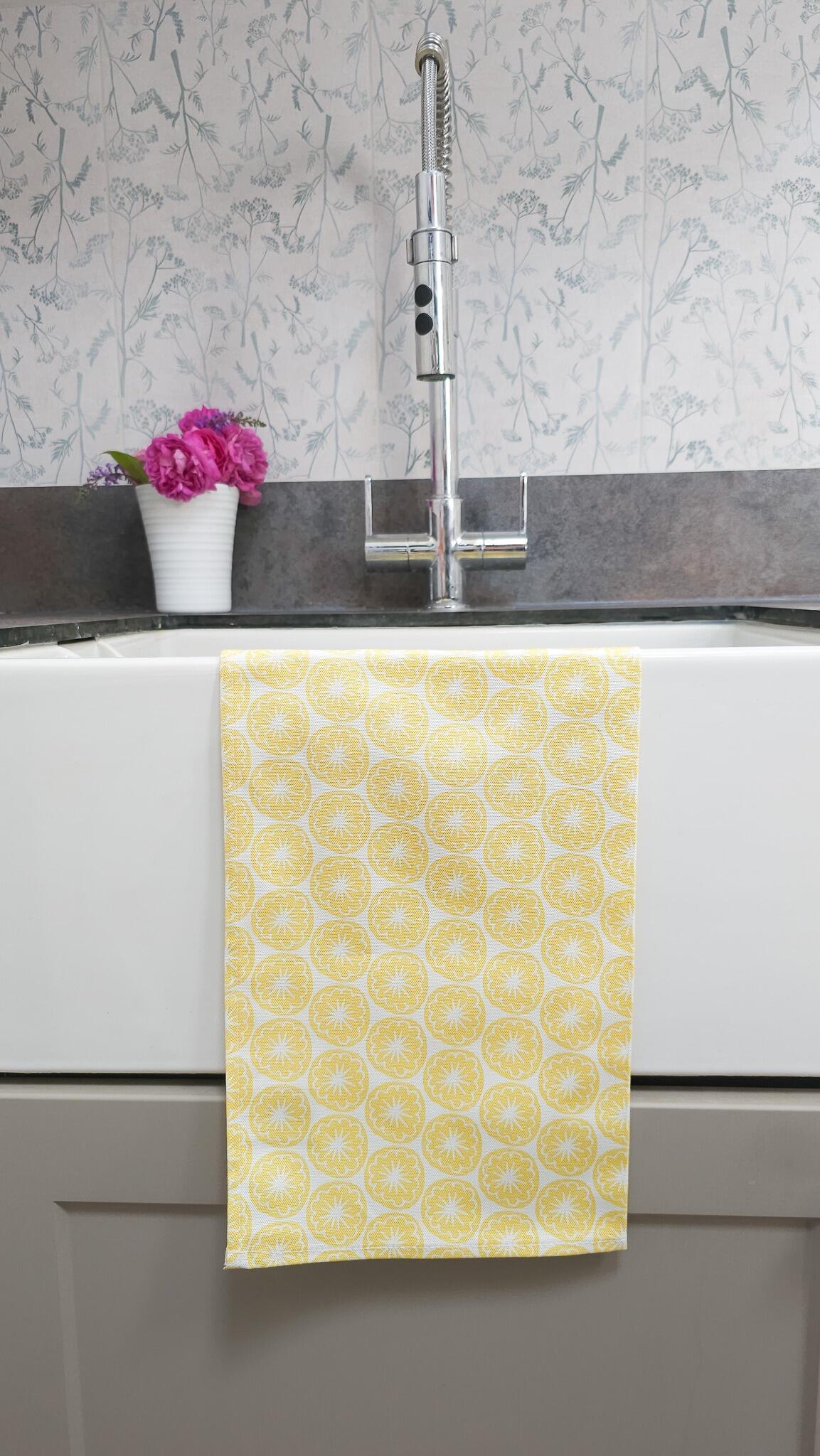 Sunshine Yellow, Poppy Seed Head Block Print Style Tea Towel folded over a white butler sink in a utility room with tap and flowers